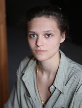 Portrait of a young woman with dark hair tied up, a grey shirt and a shimmering gold necklace